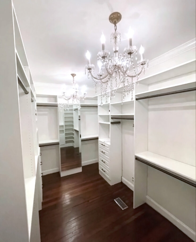 A Custom Closets of Georgia walk in closet with white cabinetry, bronze hardware, mirrored door, and hardwood floors