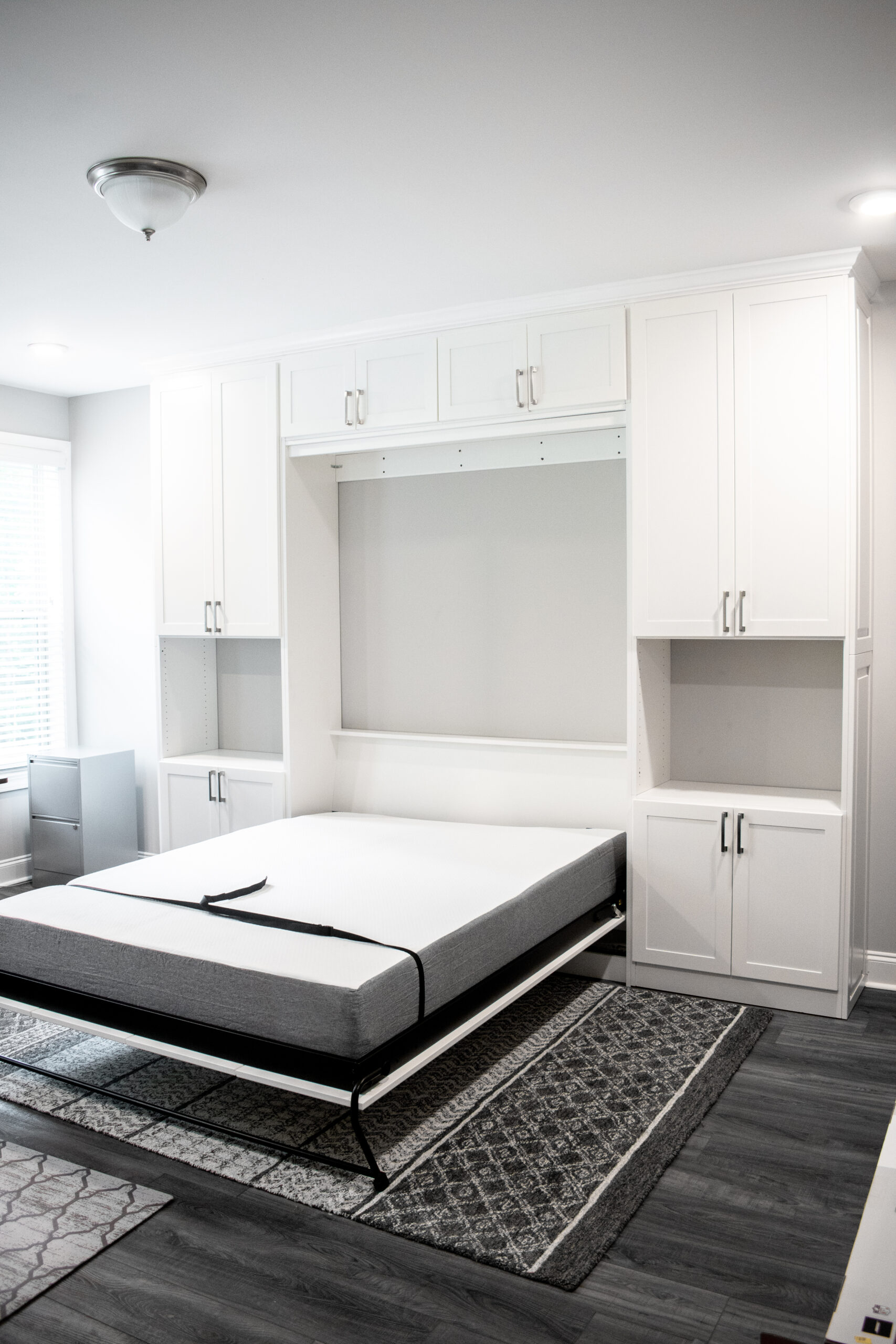 White shaker murphy bed by Custom Closets of GA. It features decorative side panels, overhead cabinets, and lower cabinets with landing spaces, and it is designed for a full-size mattress.