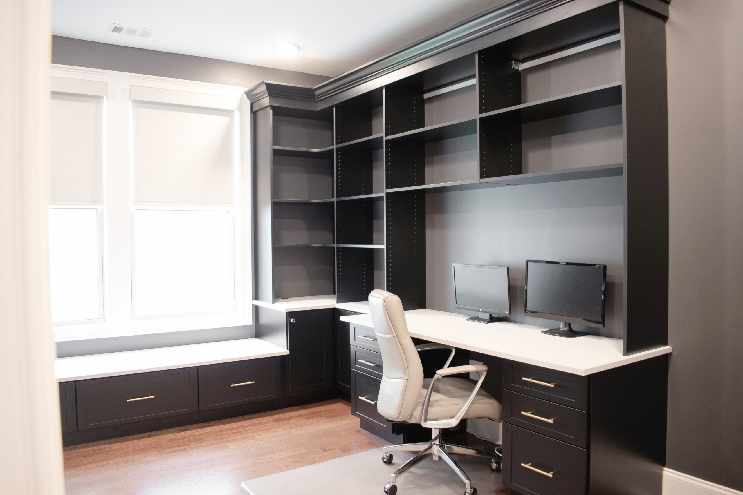 Custom black wraparound desk with bookshelves, a bench, file drawers, normal drawers, crown molding, cabinets, and a white countertop.