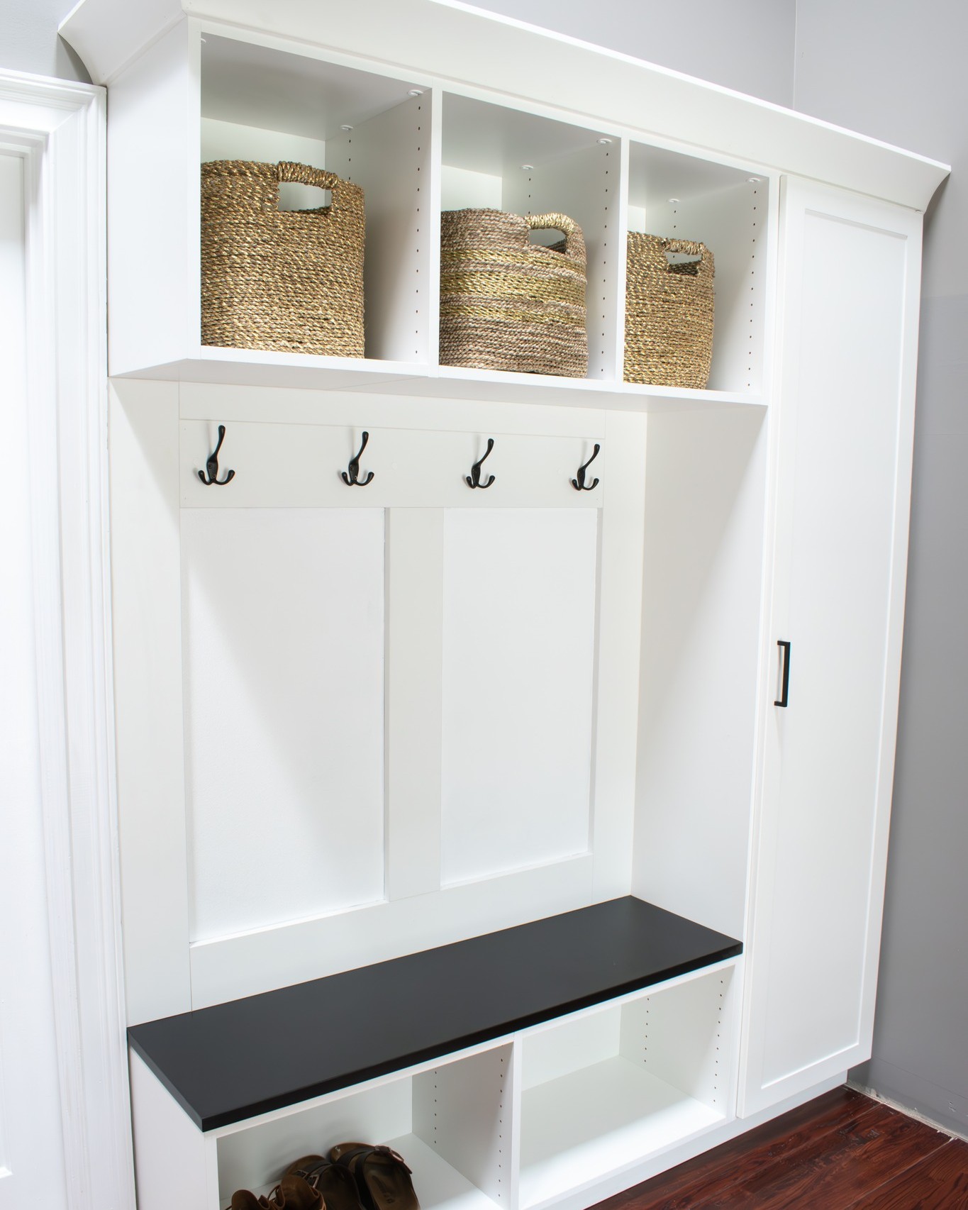 Custom Closets of GA built-in mudroom with flat-front cabinets and drawers, a bench, and coat hooks. This Palmetto, Georgia, mudroom was designed with our white material and black hardware.